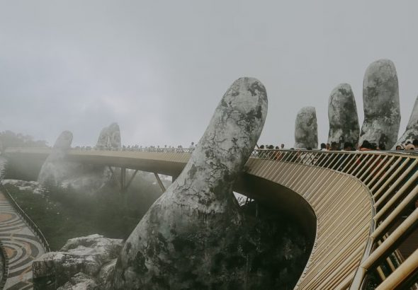Stunning view of Golden Bridge held by stone hands enveloped in mist, Ba Na Hills.